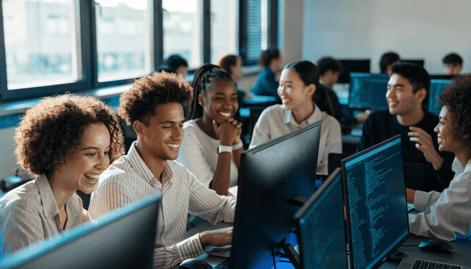 Diverse students smiling and collaborating while writing code at computers in a bright modern lab