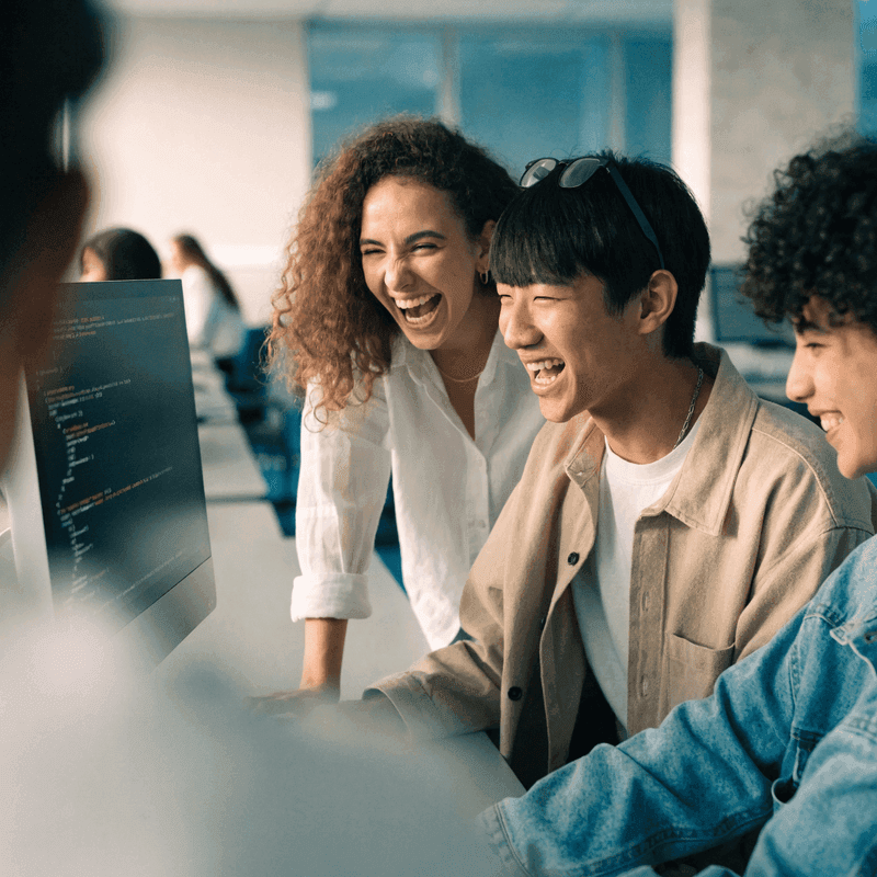 A small group of students smiling and working together at a computer in a bright lab